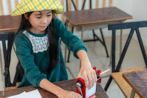 Little cute kid asian girl smile using pencil sharpener while sitting in classroom Asian children elementary school student sharpening pencils for preparing for study in next class, education concept