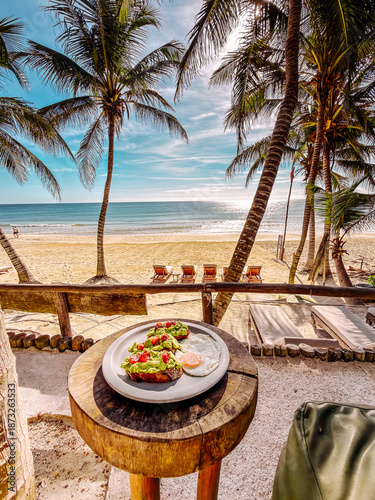 Photography Tropical beachfront breakfast scene in Tulum, Mexico, featuring avocado toast and a sunny-side-up egg served on a rustic wooden table overlooking a sandy beach and calm Caribbean Sea