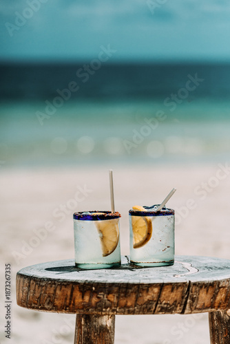 Two margarita cocktails on a rustic table by the beach in Tulum
