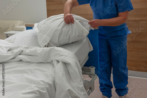 Nurse arranges blankets and pillows on a hospital bed