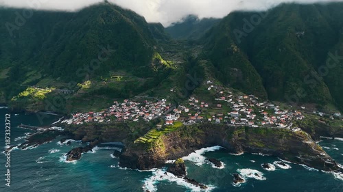 Seixal coastline with residential area, terraced hillsides, and rugged volcanic rocks. Atlantic coast of Madeira Island at sunset