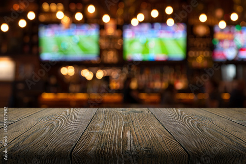 Tableau sur toile A natural wood table and a blurred background of a sports bar with screens and f