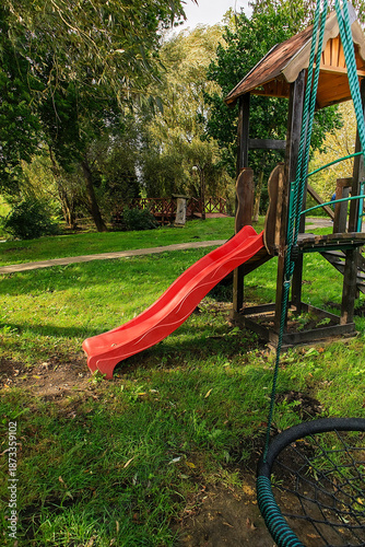 Playground with red slide, placed in a green park for children's leisure and physical activity.