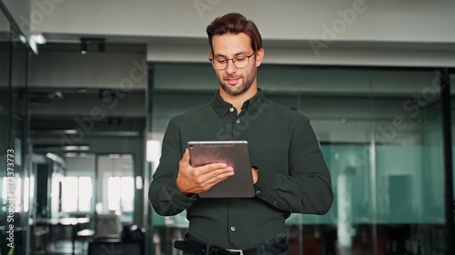 Focused European young businessman entrepreneur working on touchscreen computer device. Latin hispanic ceo business man ceo manager using tablet pad computer in office, looking at screen typing