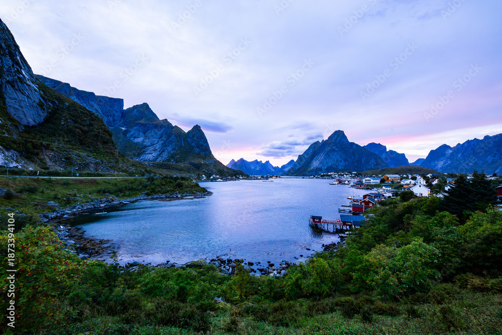 Obraz premium Autumn sunset in Reine, Lofoten Islands, Norway, with dramatic mountains, calm waters, and traditional houses along the shore.