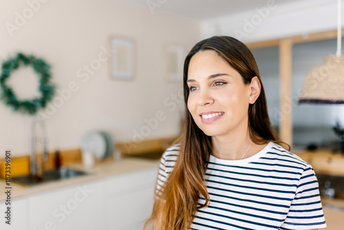 Free Download Young woman smiling while looking away, enjoying daily life moments in a bright, contemporary domestic kitchen, representing happiness, well-being, and modern lifestyle - GFXLoad