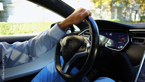 Fotografía Male hand of businessman holds steering wheel while driving electrical vehicle at city