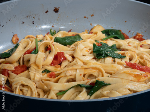 Fotografie Freshly cooked fettuccine pasta with spinach and cherry tomatoes in a pan