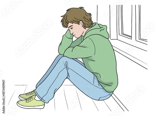 A young man sits alone on the floor, looking sad and depressed near a window.