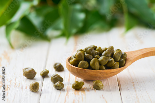 Schilderij op canvas wooden spoon with pickled caper berries on a light kitchen table, selective focus