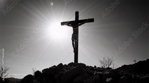 Silhouette of Jesus Christ on the cross with a bright sunburst. Black and white crucifixion scene on a rocky hill. Religious faith and sacrifice concept. Cinematic monochrome footage