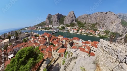 Aerial view of Mirabella fortress walls of Omis town, historic fort, features a Croatian flag waving atop its battlements, overlooking the scenic Omis coastline and vast Adriatic Sea in Croatia