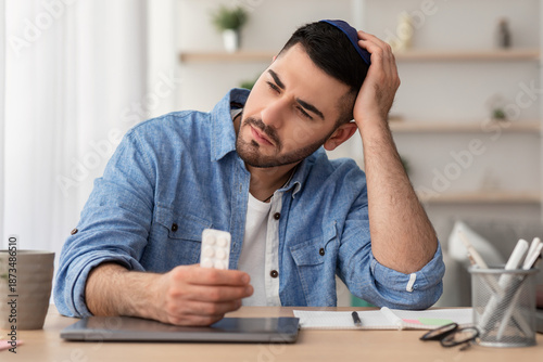 Portrait of young man feeling depressed, holding pill and looking away, thinking about his disease. Emotionally unstable millennial gyt suffering from illness, having emotional problems