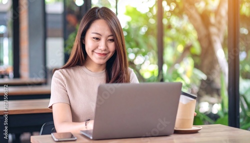 Free Download Smiling Young Asian Woman Working on Laptop in Modern Cafe or Co-working Space - GFXLoad