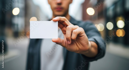 Young adult in casual attire holding up a blank white credit or ID card toward the camera