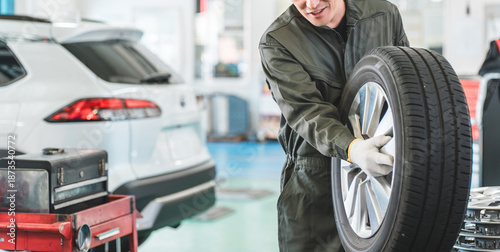 Fotografie Male mechanic carrying tires at an auto repair shop (physical labor, hard work,