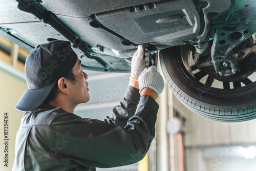 Fotografie A male car mechanic performing maintenance, inspection and work under a vehicle