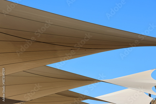 Fotografie Beige shade sails canopy against a blue sky abstract background
