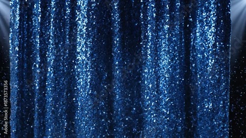 A blue sequined curtain is lit by stage lights, sparkling against a dark background