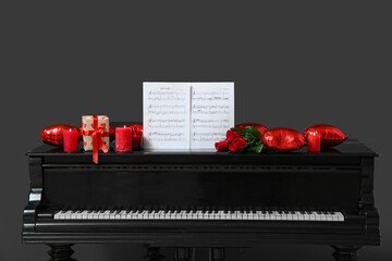 Piano with note sheets, burning candles, roses and balloons on dark background. Valentine's Day celebration