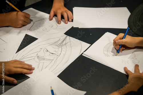 A bunch of children's hands drawing characters with lead pencils, viewed from above - horizontal