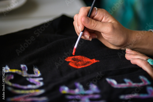 A hand holding a paint brush painting a red heart onto a tee shirt - horizontal