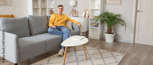 Young man sitting on grey sofa in living room