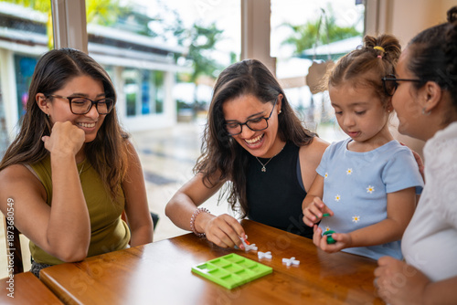 Women and girl smiling and playing game together at coffee shop