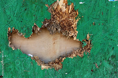 Background, texture of a fence element made of OSB board painted green with a punched hole patched with plywood