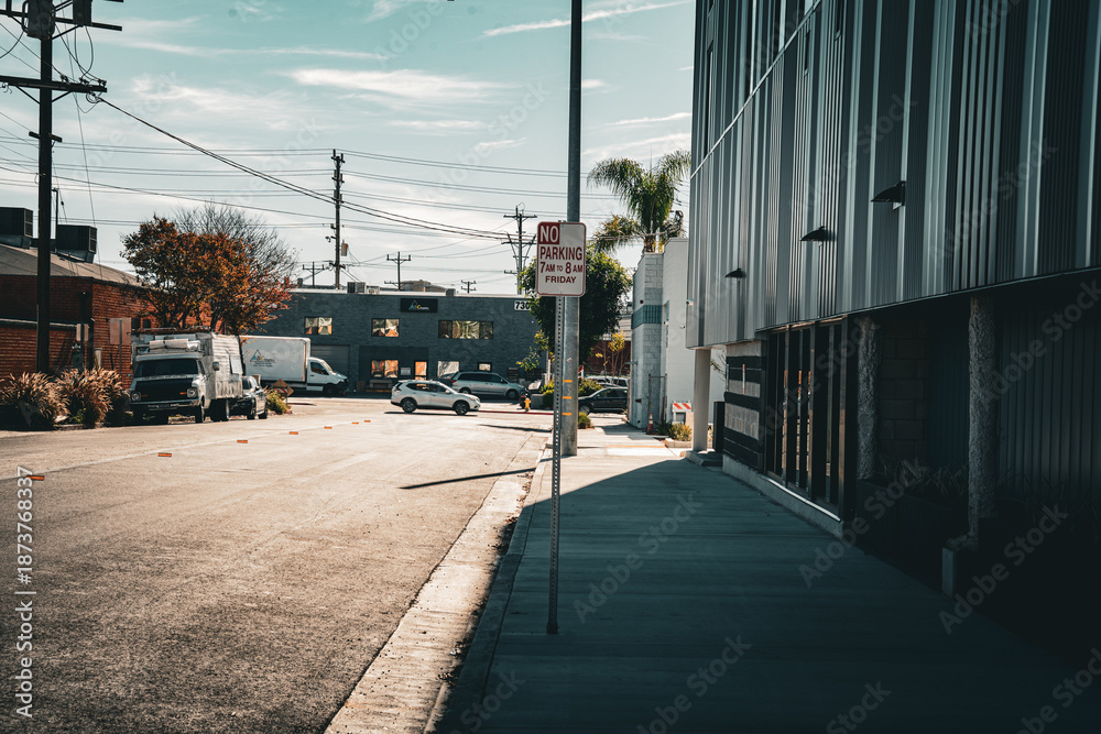 Obraz premium Sunny urban street scene with modern building and parked vehicles