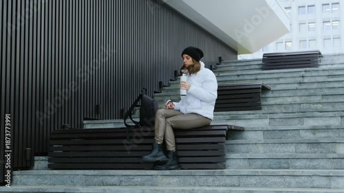 Woman Sitting on Park Stairs Drinking Tea from Thermos. Urban Relaxation.