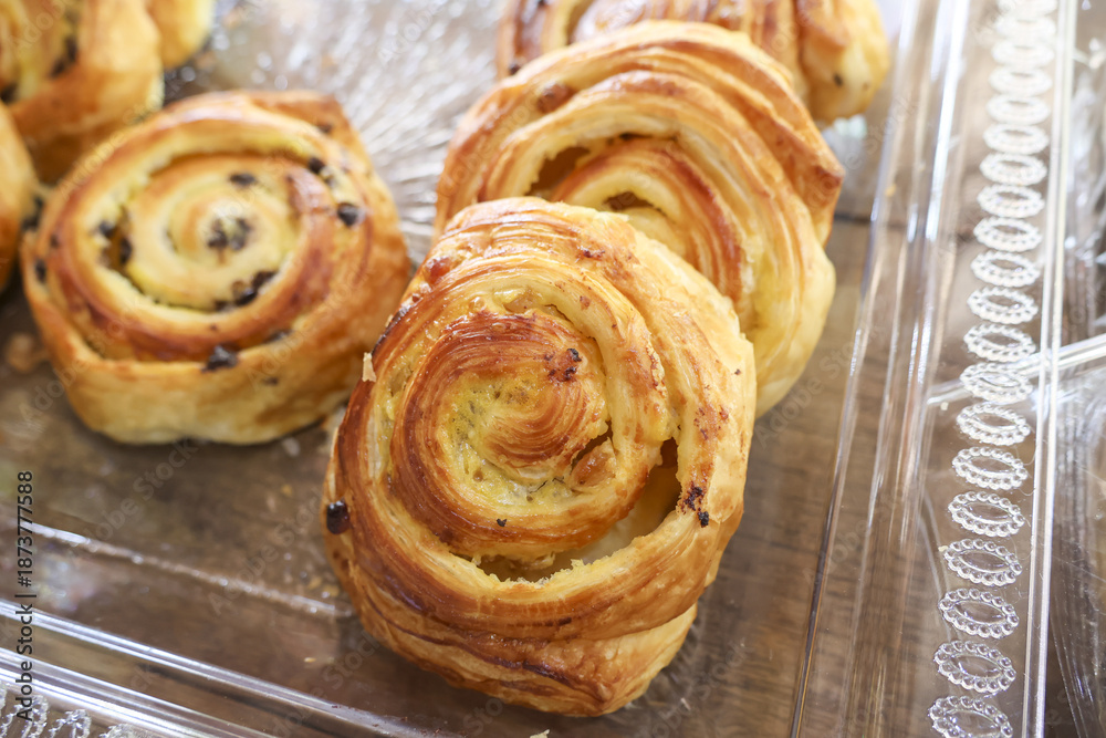 Fototapeta premium Delicious freshly baked raisin swirl danish pastries displayed beautifully on transparent tray evoking sense of warm comforting morning breakfast treat at local bakery shop