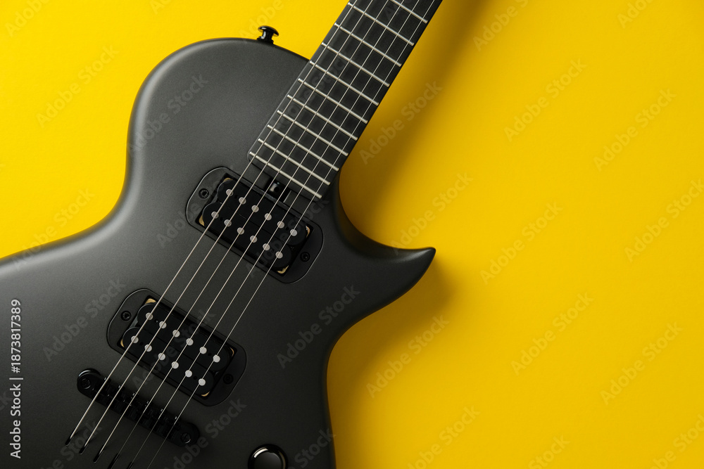 Obraz premium Stylish black electric guitar on a vibrant yellow background, top view.