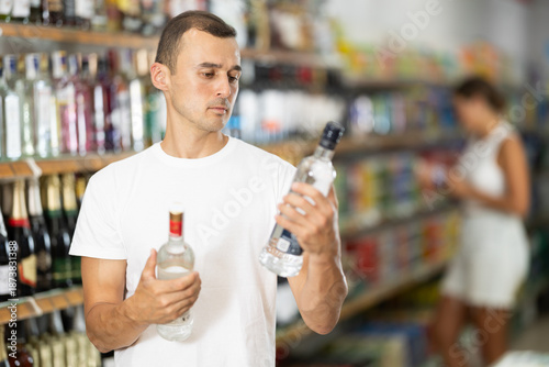 Wallpaper Mural Young male shopper in casual clothes chooses vodka in grocery store Torontodigital.ca