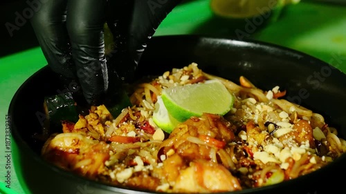 Cook finishes aroma pad thai noodles with prawns and peanuts. Chef places warm zucchini chunks before pressing lime wedge over dish top