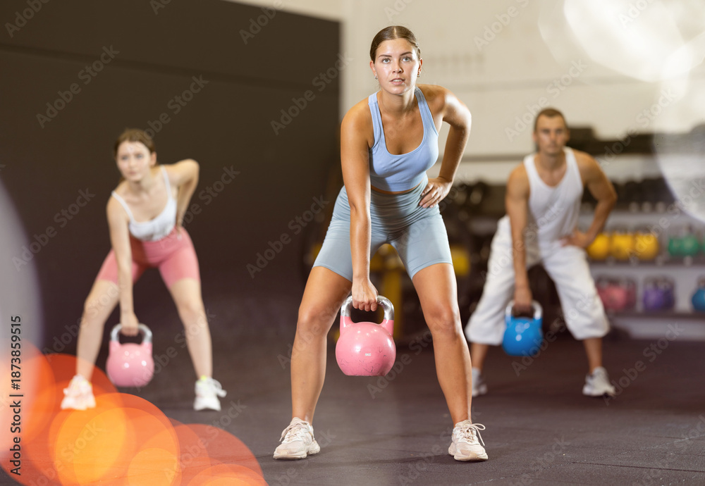 Obraz premium Young athletic woman lifting heavy kettlebell in gym