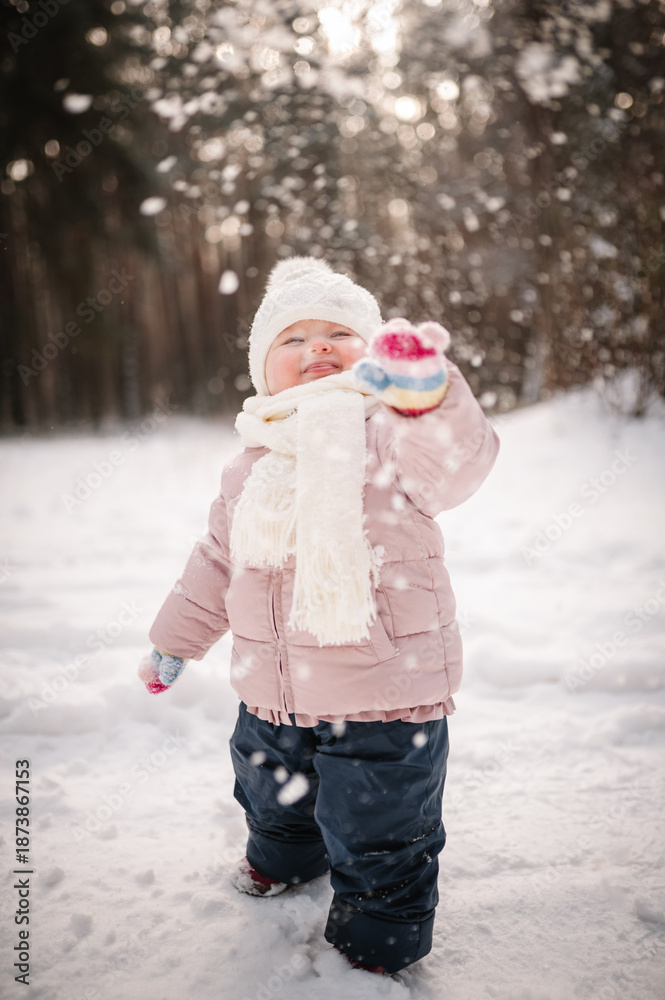 Naklejka premium Snowfall. Kid enjoying and walking in a snowy forest. Happy family holidays. Little girl standing in winter park. Portrait of a cute child having fun and playing with snow. Frosty winter season.