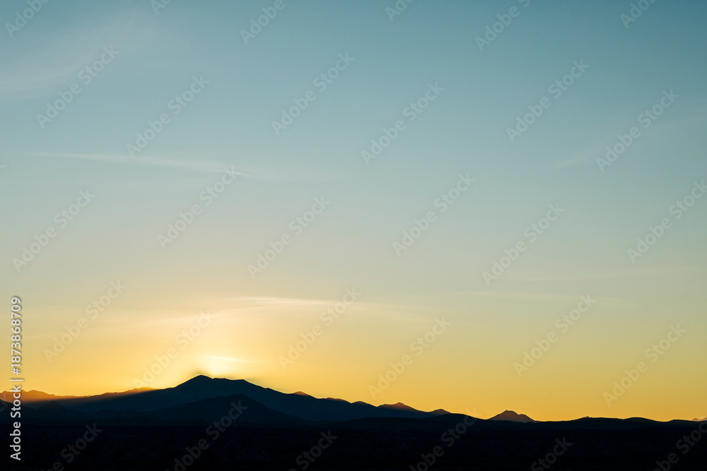 Naklejka premium Sun setting behind silhouetted mountain landscape