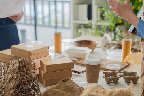 Asian entrepreneurs team in sustainable workshop discussing eco-friendly biodegradable packaging, holding molded pulp trays and kraft boxes,creative green business startup collaboration bright room
