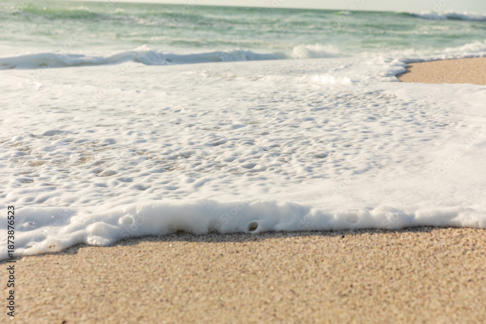 Fototapeta premium White sea foam with wave splashing on shore at beach on sunny day