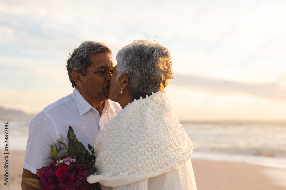 Fototapeta premium Newlywed senior multiracial couple kissing each other during wedding ceremony at beach