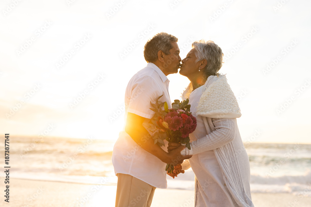 Fototapeta premium Side view of senior multiracial couple kissing each other during wedding ceremony at beach