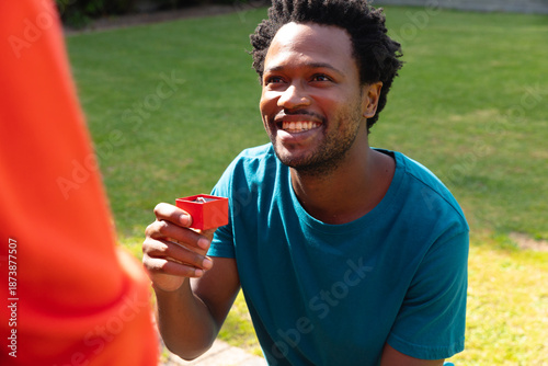 Foto Smiling young african american man proposing girlfriend with engagement ring in