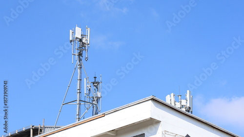 Cell tower on the roof of a building. Macro base station or base transmitter, telecommunications station with antennas of 4G and 5G cellular against blue background. Selective focus