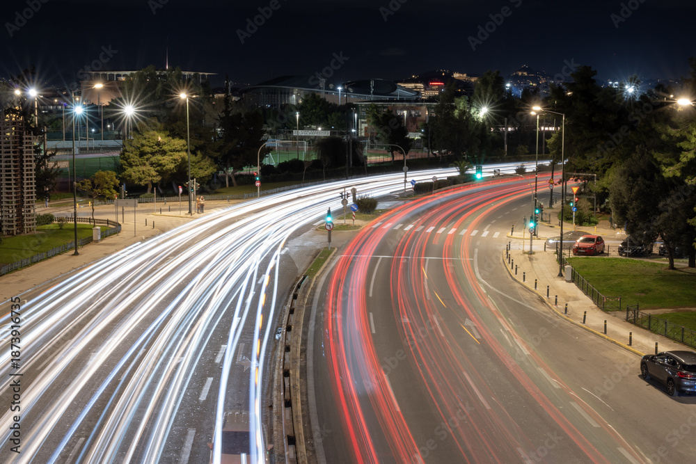 Obraz premium Night city traffic captured with long exposure showing dynamic light trails on a wide urban road in Athens, Greece. Modern transport, motion, speed and city life concept.
