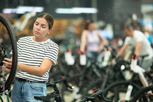 Billede på lærred Young woman buyer chooses bicycle in sports store