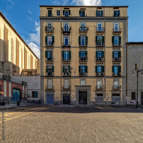 Traditional yellow residential apartment building with green shutters at Piazza del Gesù Nuovo in Naples. Travel in south Italy.