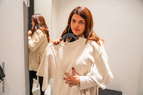Woman trying on clothes in fitting room while standing in front of mirror inside fashion store, Shopping experience, personal style choice and consumer decision process in real life retail environment