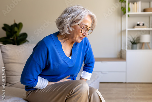 Foto Senior woman suffering from abdominal pain while sitting on sofa at home