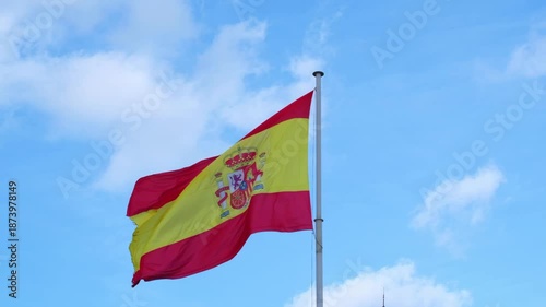 Low angle view of the national flag of Spain waving proudly in the wind against a bright blue sky with white clouds
